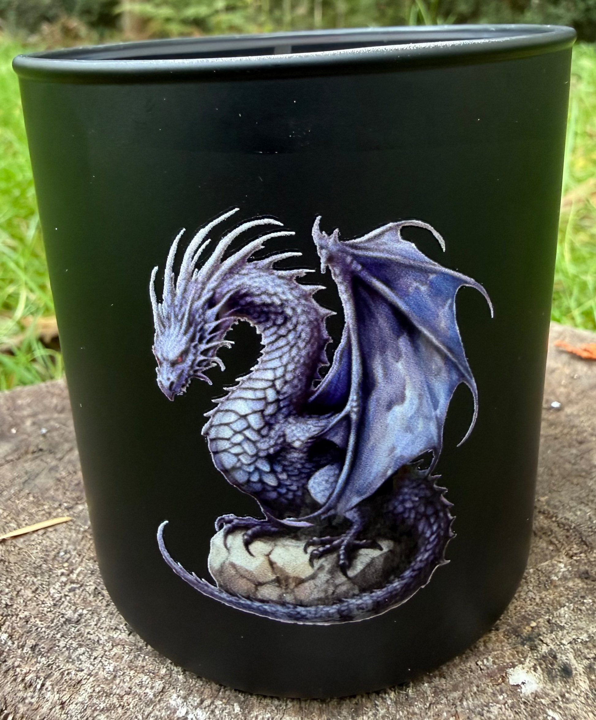 Black candle with a dragon design on a stone surface with grass and trees in the background