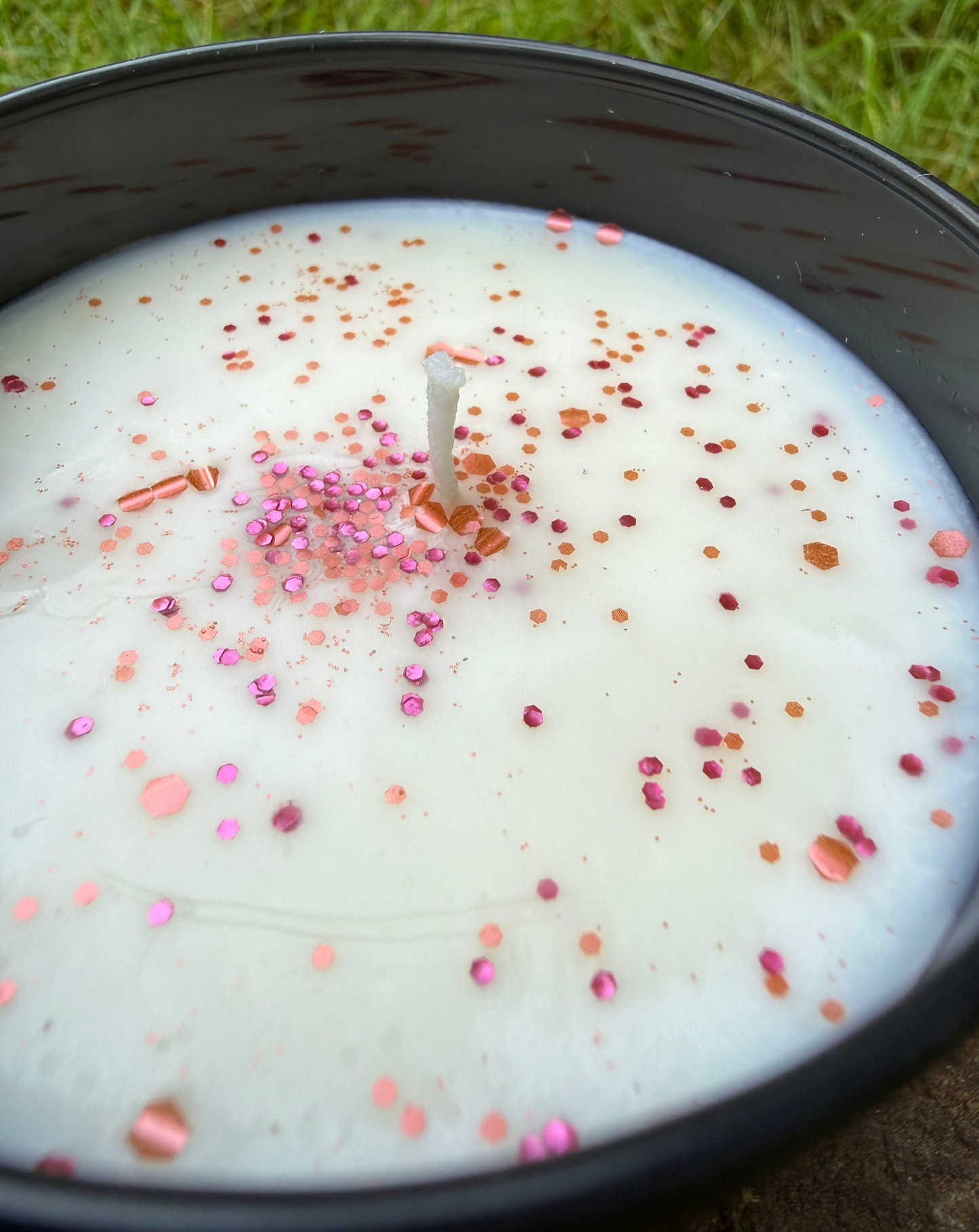 Candle with colorful sprinkles in a black container on grass