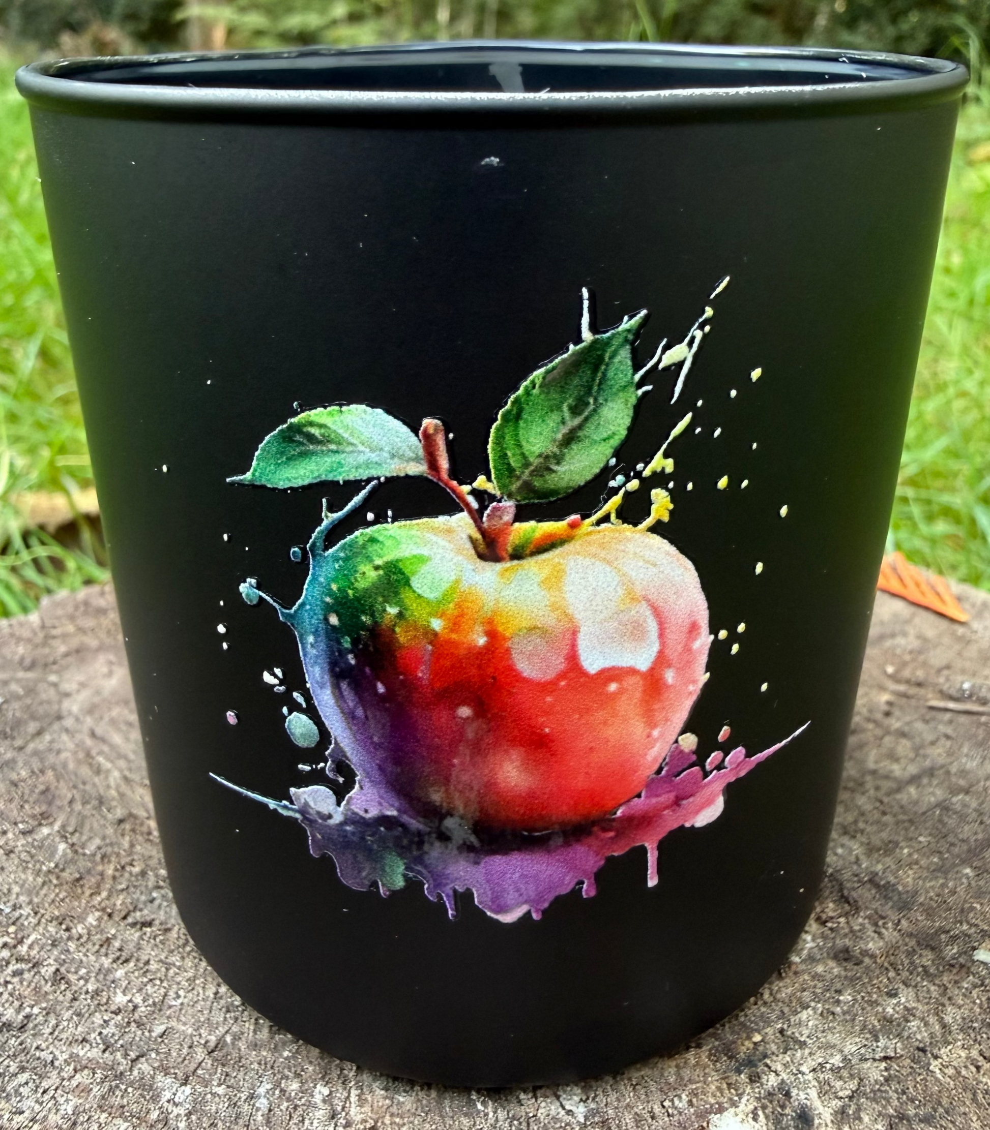 Black candle with a colorful apple design on a stone surface outdoors