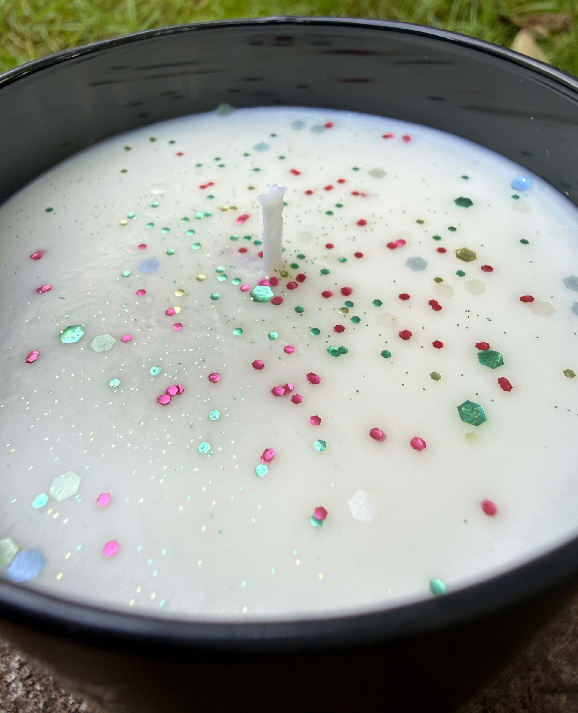 Candle with colorful sprinkles in a black container on grass