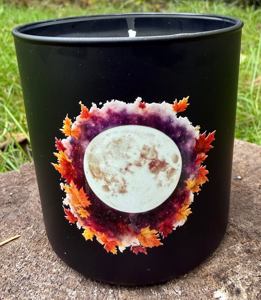 Black candle with a moon and leaf design on a stone surface with a natural background