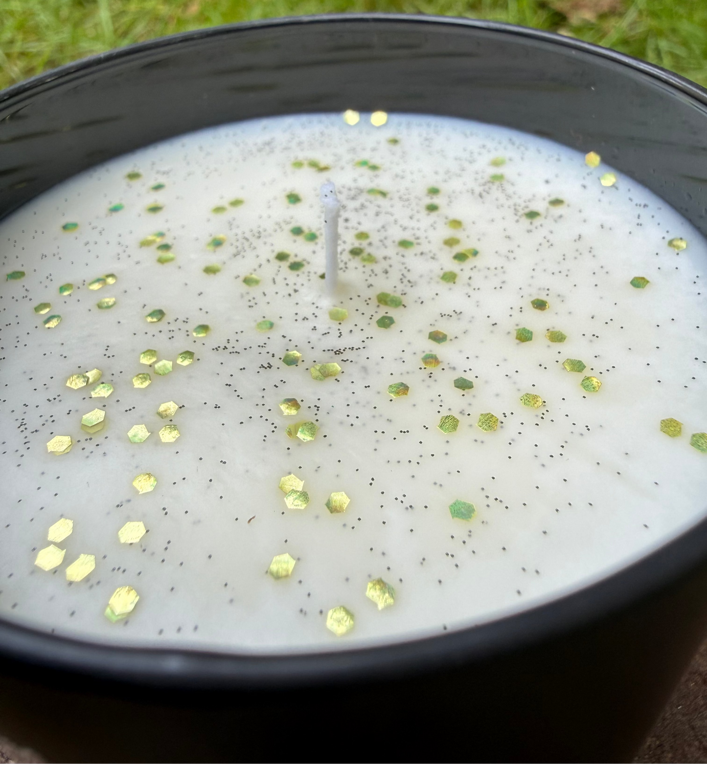 Candle with decorative elements in a black container on grass