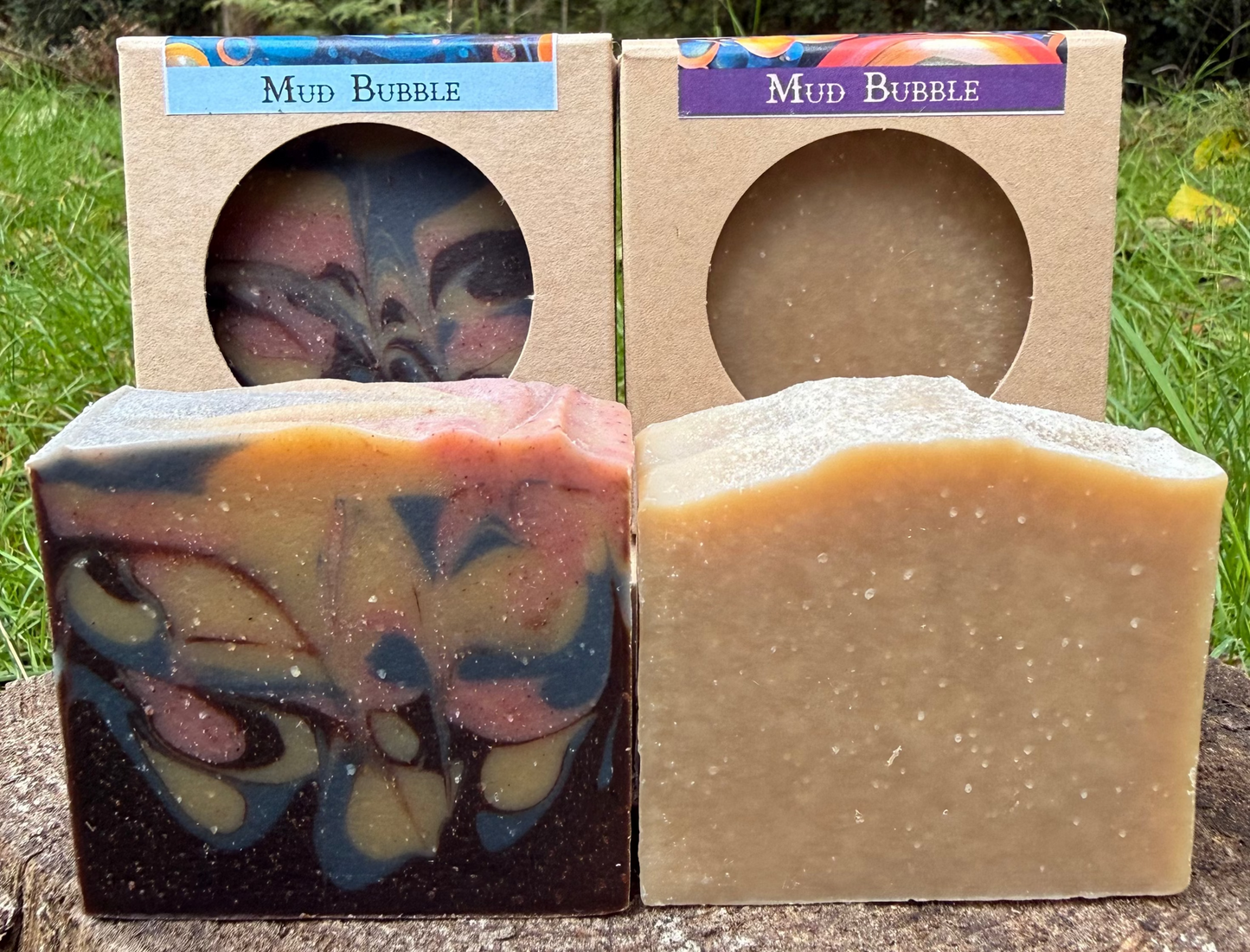 Two bars of soap with 'Mud Bubble' packaging in a natural setting.