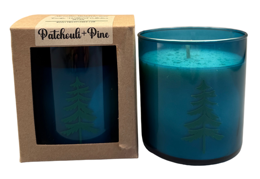 teal glass candle with tree design in a brown box labeled 'Patchouli + Pine'  on a white background