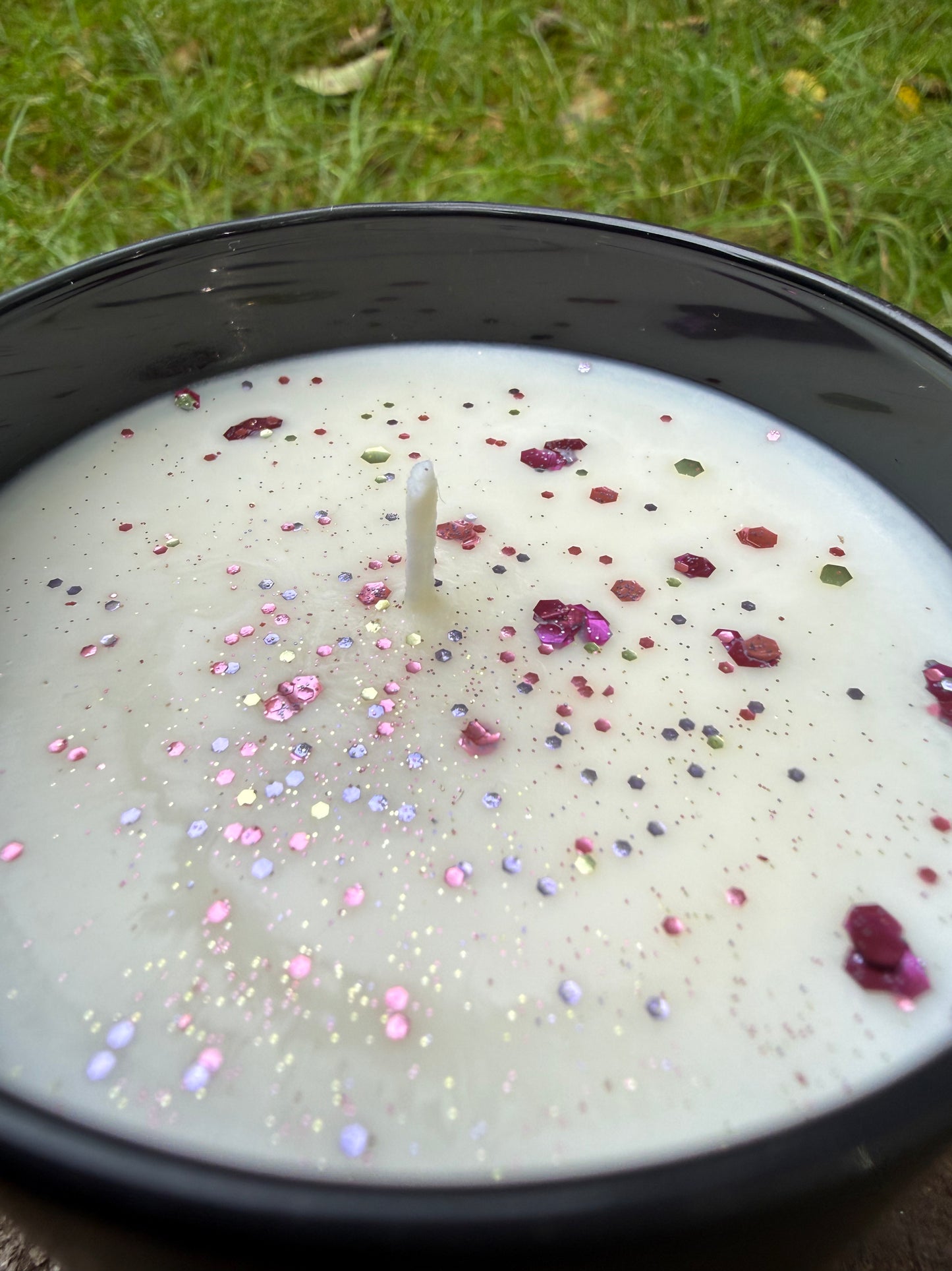 White candle with colorful sprinkles in a black container on grass