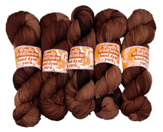 Five skeins of brown yarn with labels on a light gray background