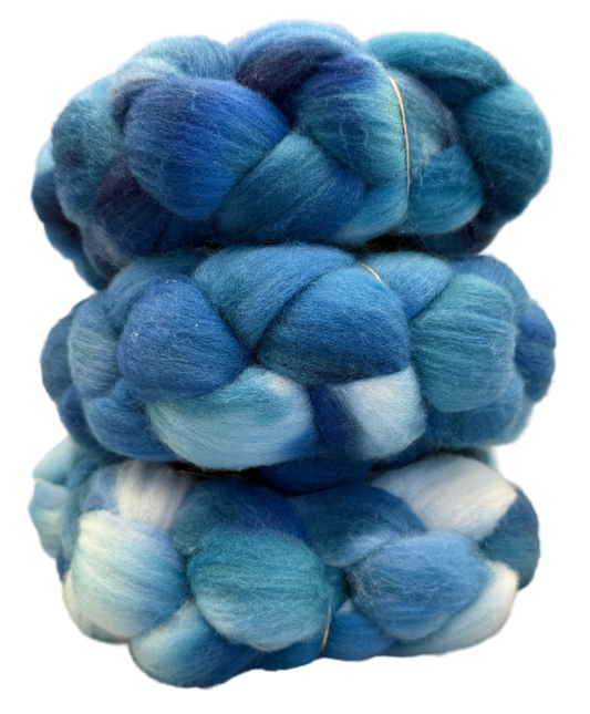Three skeins of blue and greens fiber  stacked on a beige background