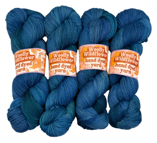 Four blue skeins of yarn with 'Woolly Wildflower' labels on a light gray background