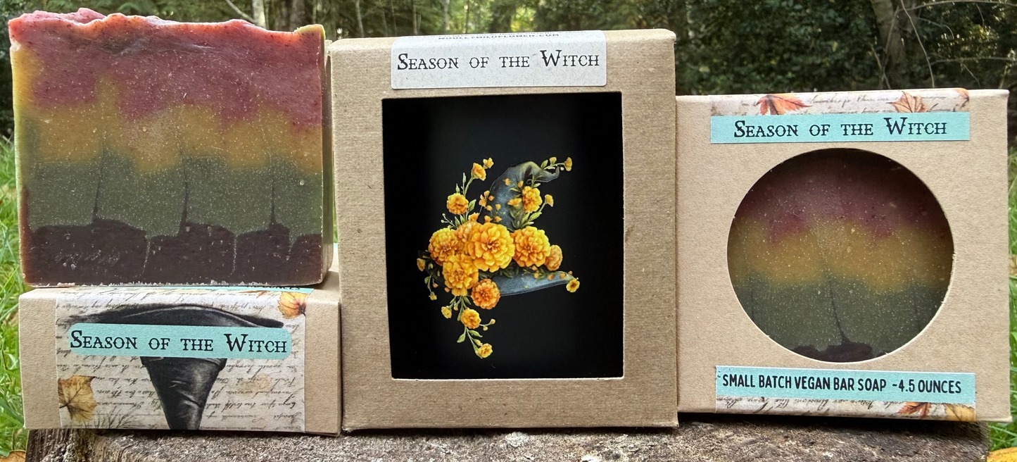 Three 'Season of the Witch' soap bars and packaging on a wooden log with a natural background.
