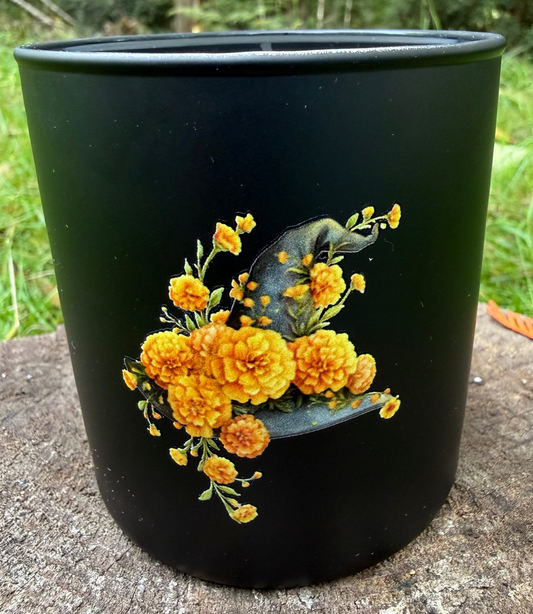 Black candle with yellow floral design on a wooden surface outdoors