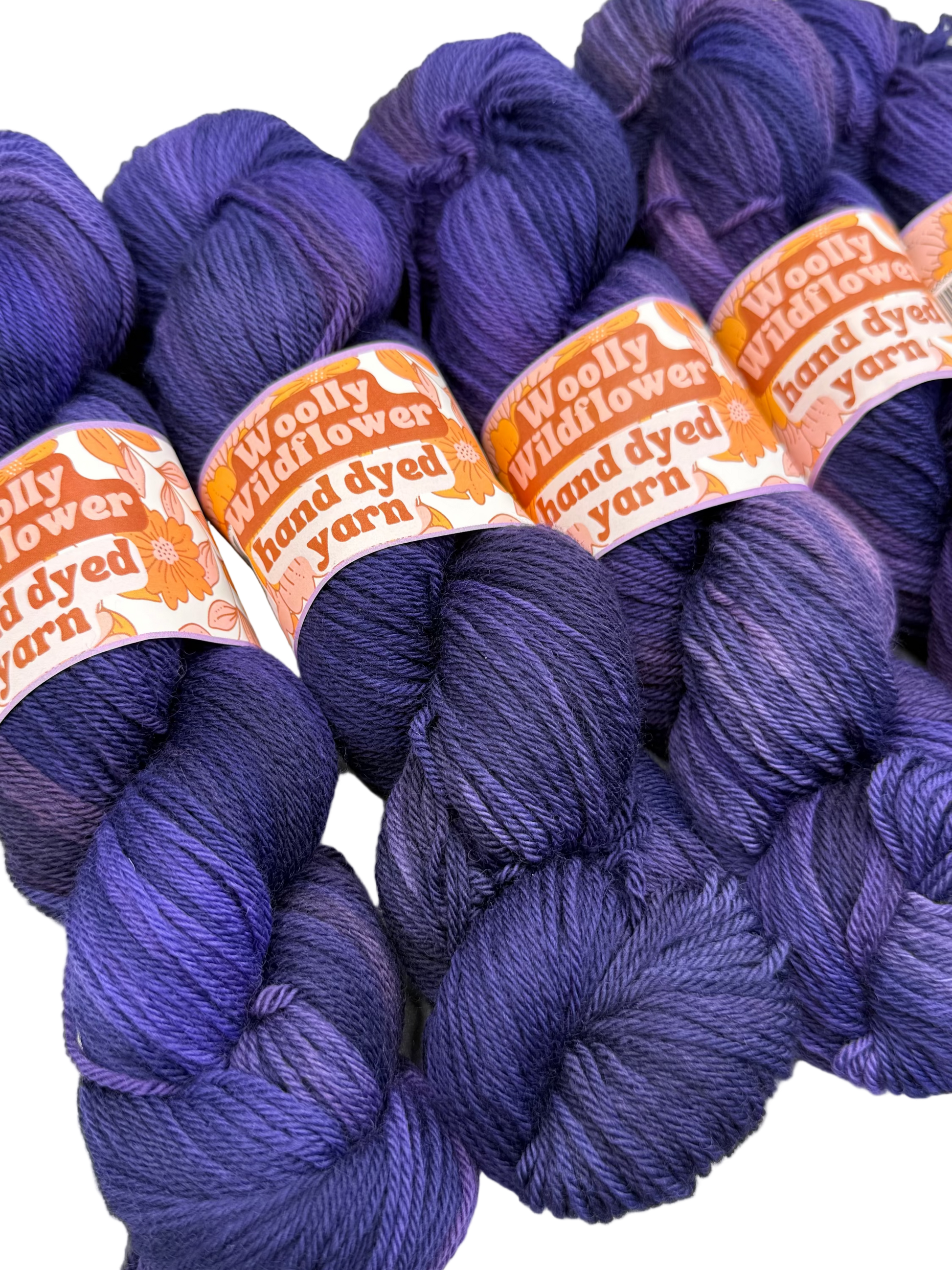 Purple yarn skeins with 'Woolly Wildflower' labels on a white background