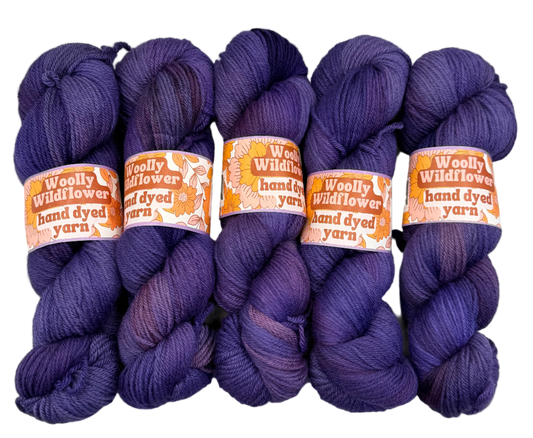 Four skeins of purple yarn with 'Woolly Wildflower' labels on a light gray background