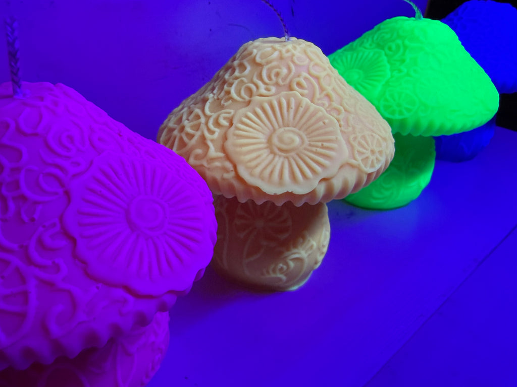 Three textured mushroom-shaped candles in neon pink, beige, and glowing green, arranged on a surface under UV light.
