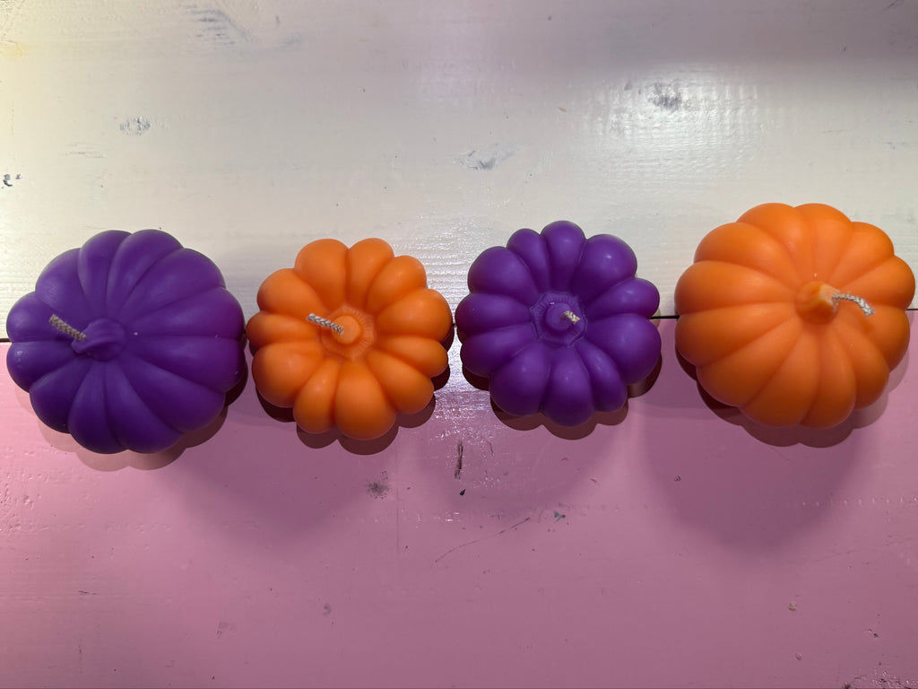 A vertical string of Halloween-style pumpkin-shaped candles in alternating orange and purple, against a pink wall.