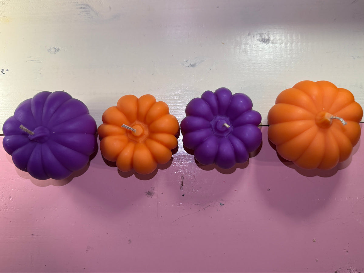 A vertical string of Halloween-style pumpkin-shaped candles in alternating orange and purple, against a pink wall.