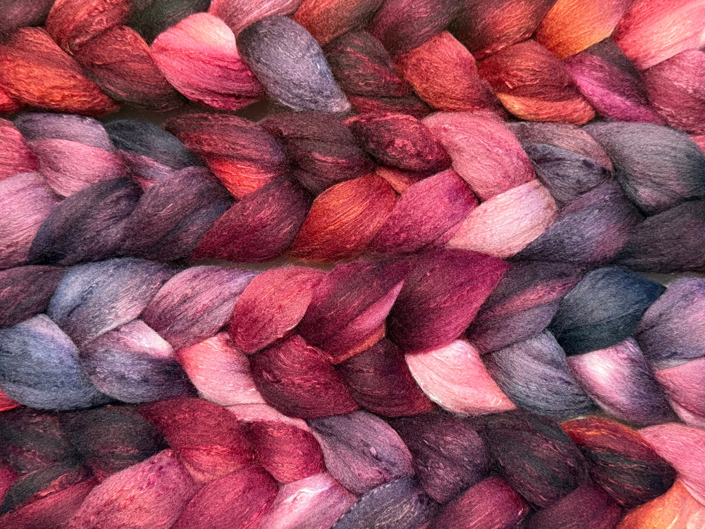 Close-up of braided yarn fibers in a variegated mix of deep pink, burgundy, plum, charcoal, and soft lavender-gray tones.