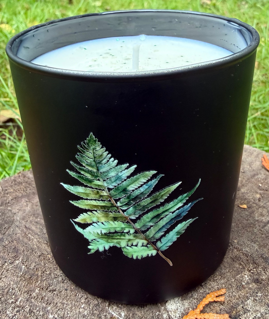 Black candle with a fern design on a stone surface outdoors