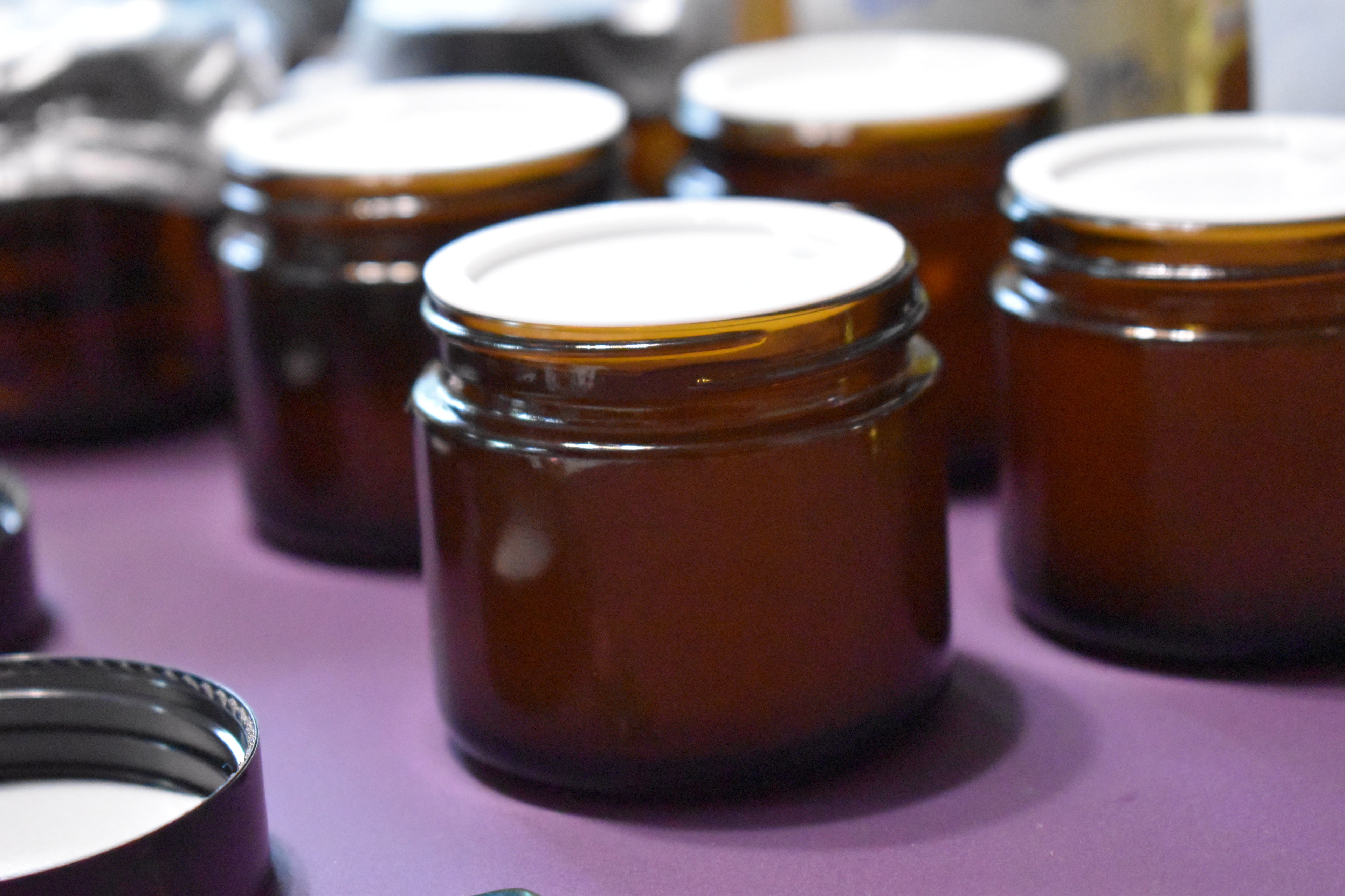 Brown glass jars with white lids on a purple surface