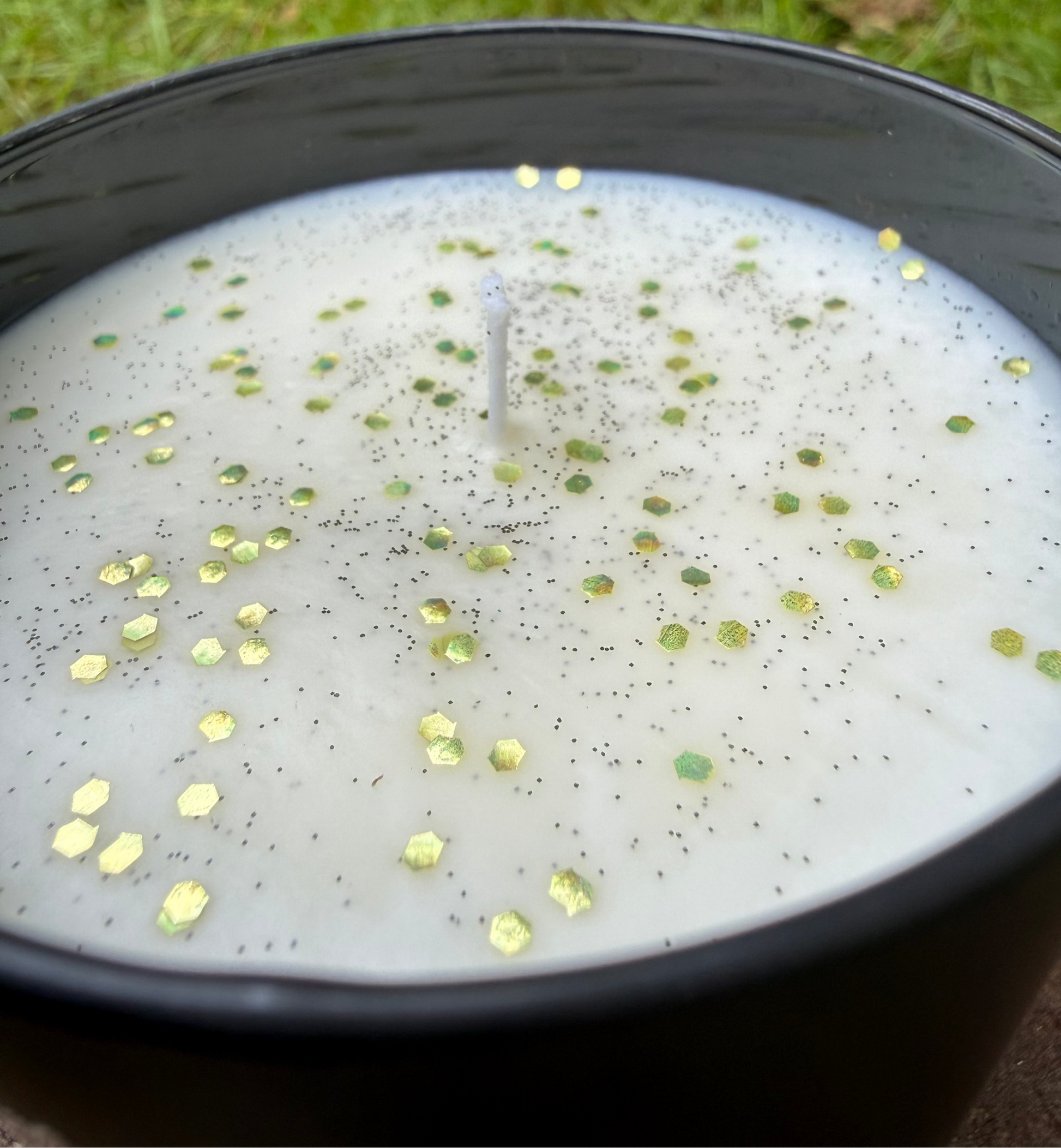Candle with decorative elements in a black container on grass