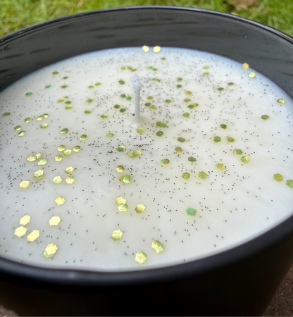 Candle with decorative elements in a black container on grass