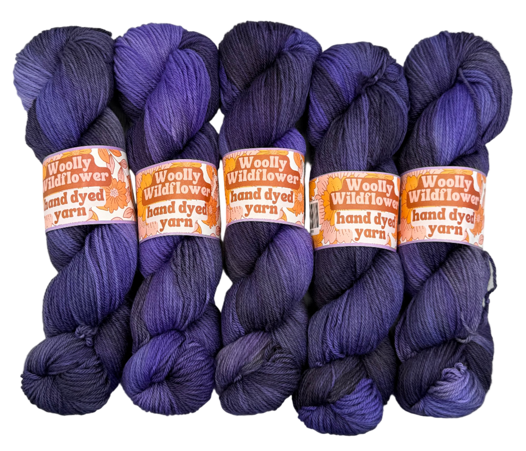 Five skeins of purple yarn with 'Woolly Wildflowers' labels on a white background