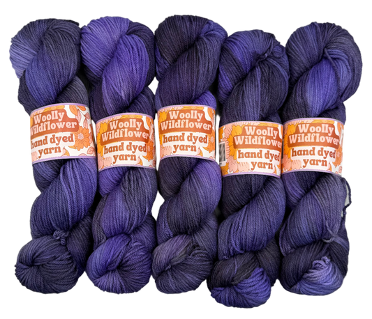 Five skeins of purple yarn with 'Woolly Wildflowers' labels on a white background