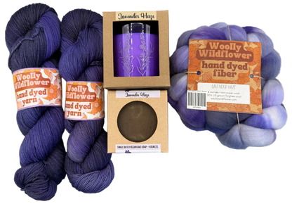 Two skeins of purple yarn, a purple tumbler, and a ball of hand-dyed fiber on a gray background.