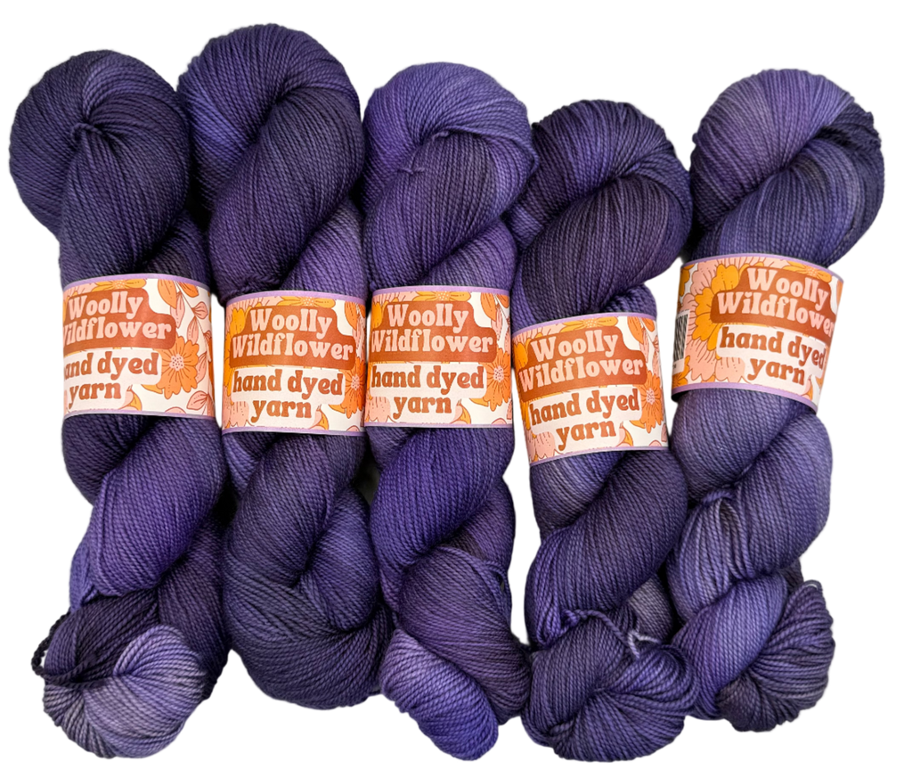 Four skeins of purple yarn with orange labels on a light gray background