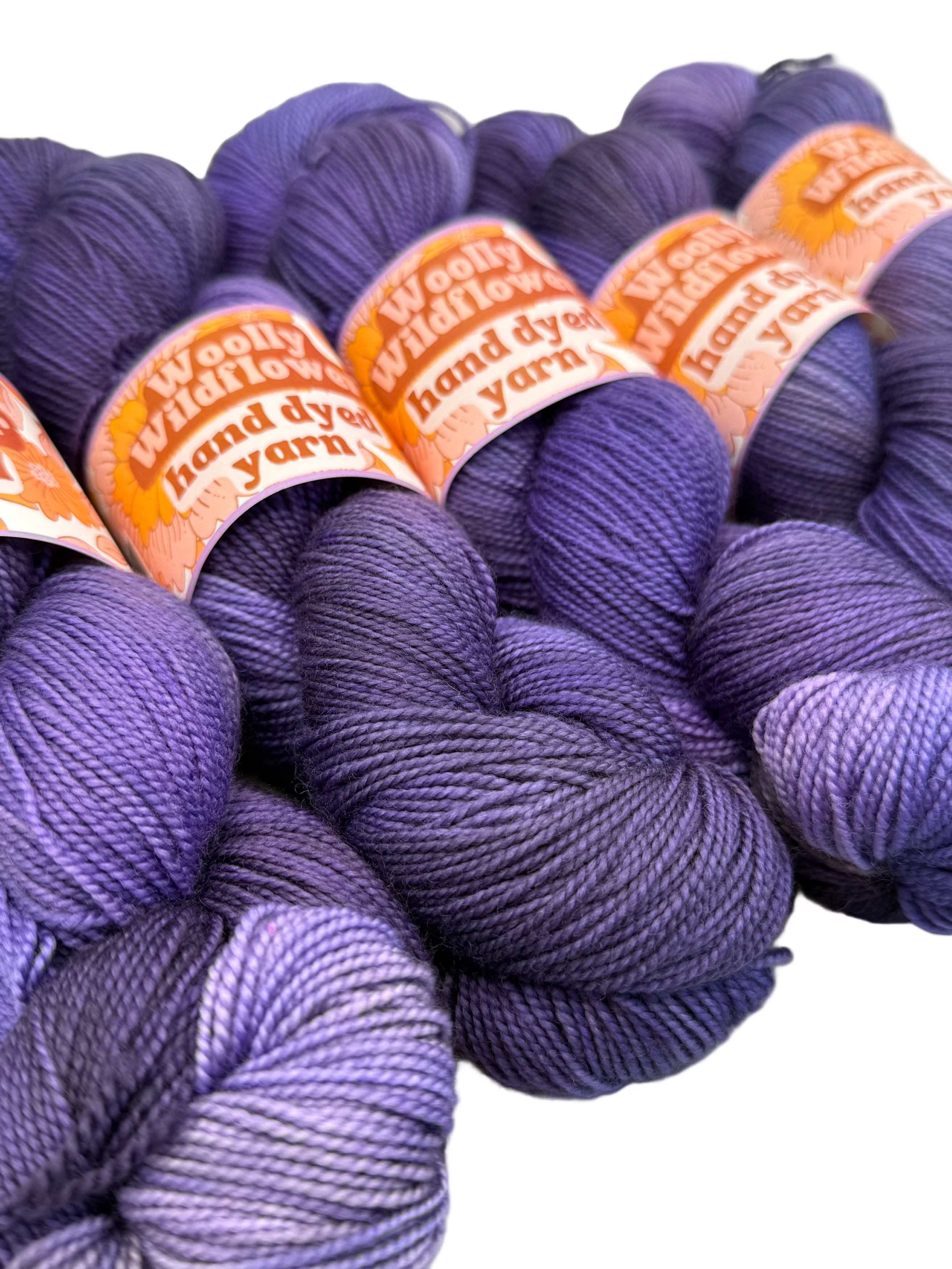 Purple yarn skeins with 'Woolly Wildflower' labels on a white background