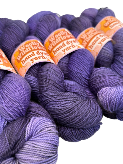 Purple yarn skeins with 'Woolly Wildflower' labels on a white background