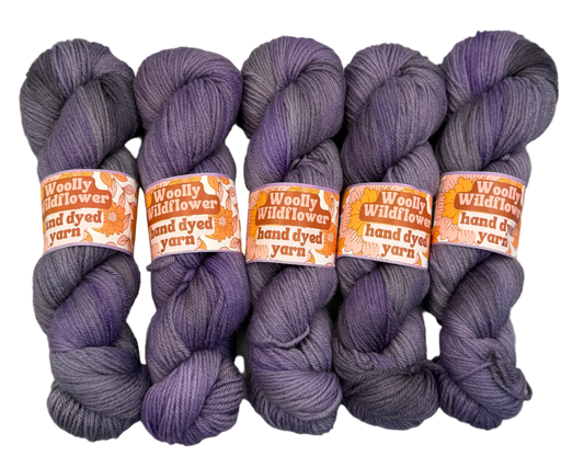 Five skeins of purple yarn with orange labels on a white background