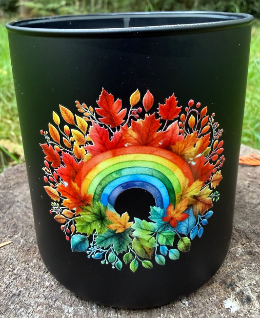 Black candle with a colorful rainbow and leaf design on a natural background