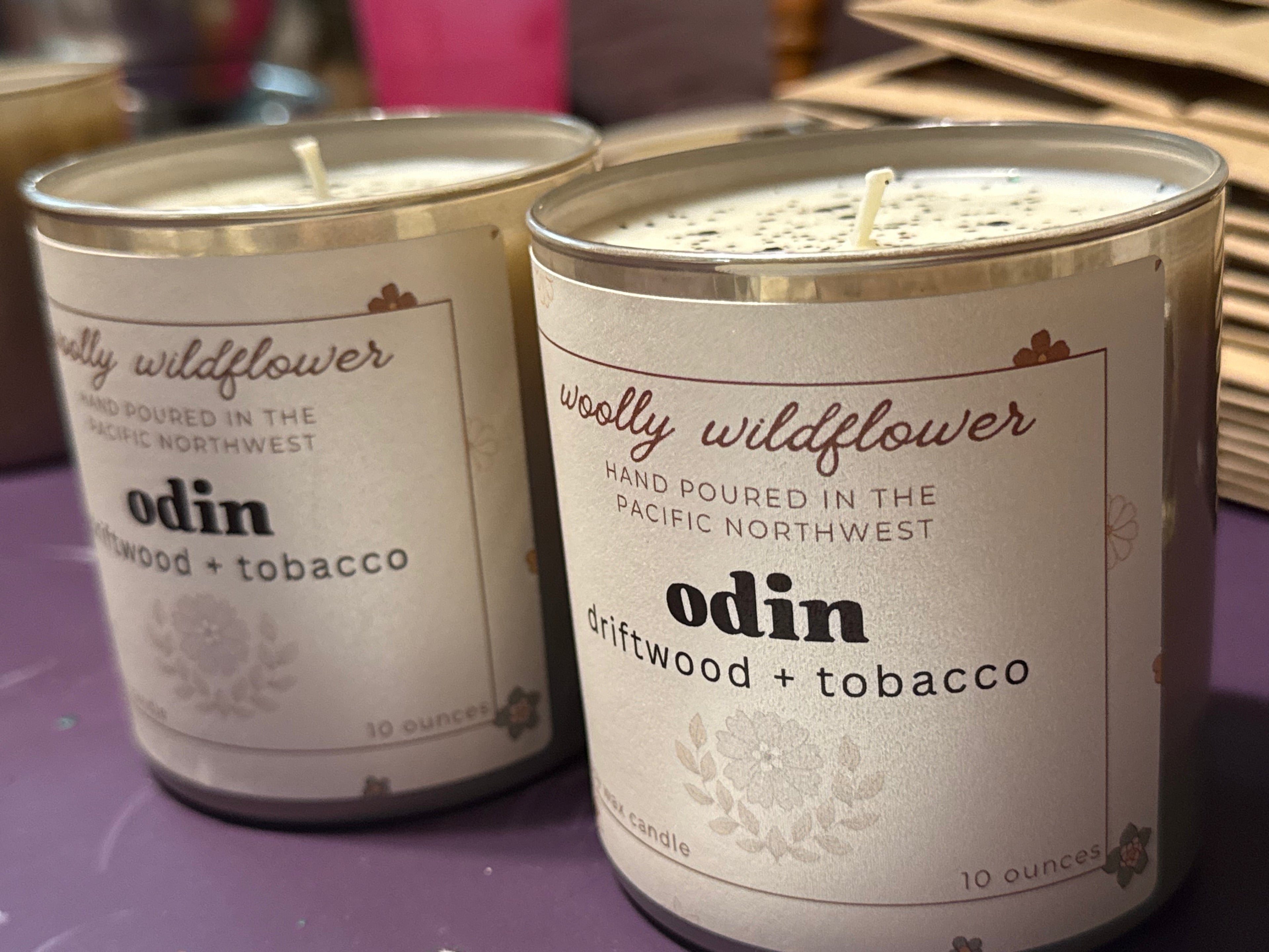 Two candles labeled 'woolly wildflower' with 'odin' scent on a purple surface.