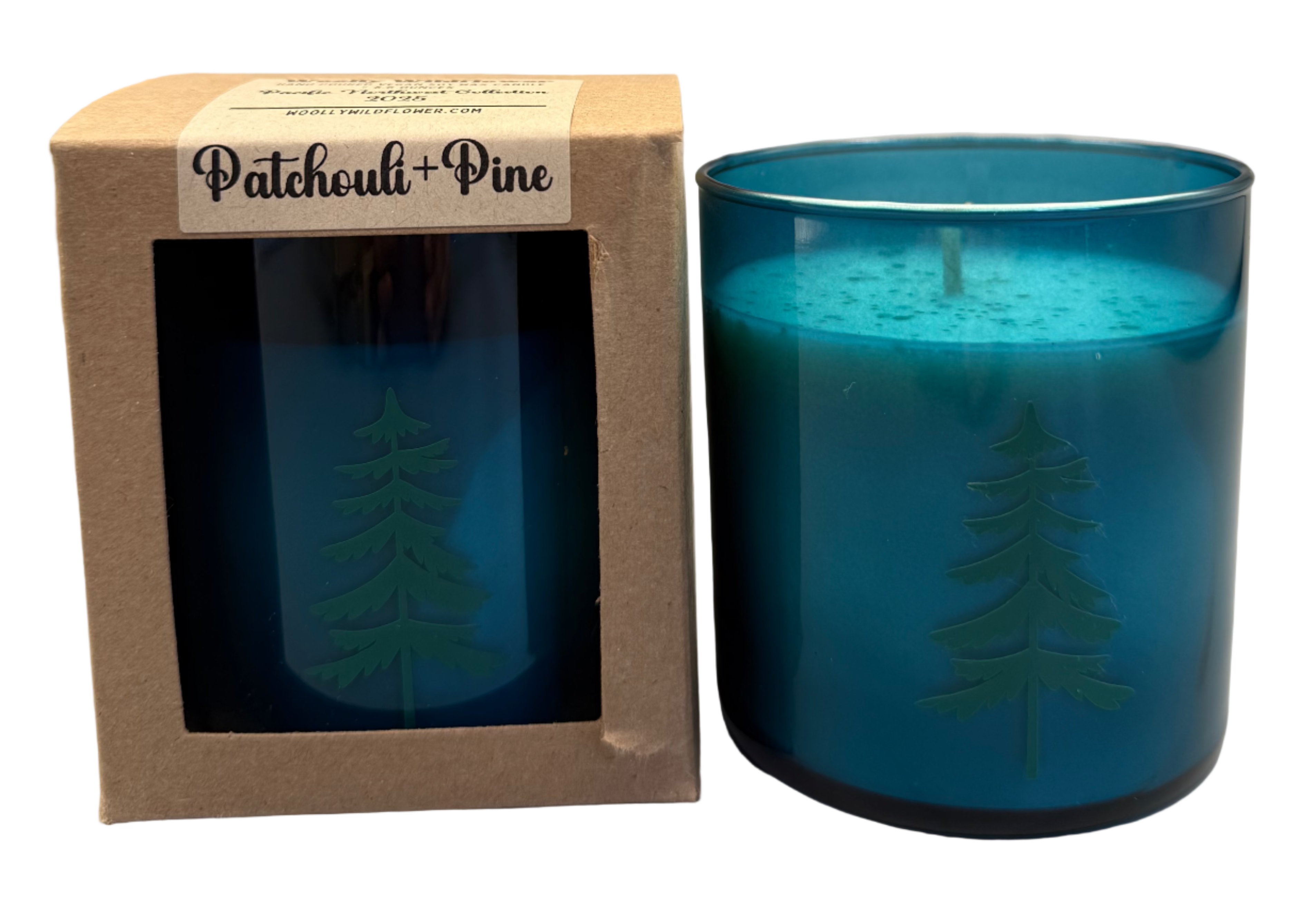 teal glass candle with tree design in a brown box labeled 'Patchouli + Pine'  on a white background