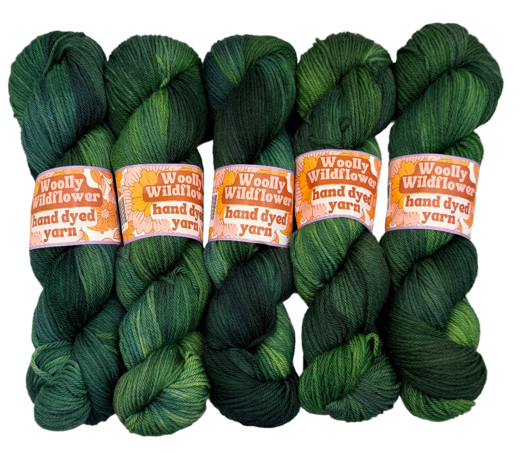 Five skeins of green hand-dyed yarn with 'Woolly Wildflower' labels on a white background.