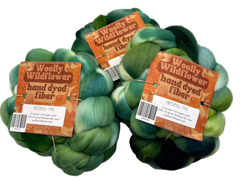 Two skeins of green hand-dyed fiber with 'Woolly Wildflower' labels on a gray background.