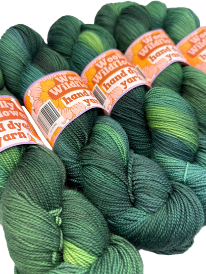 Green yarn skeins with 'Woolly Wildflower' labels on a white background