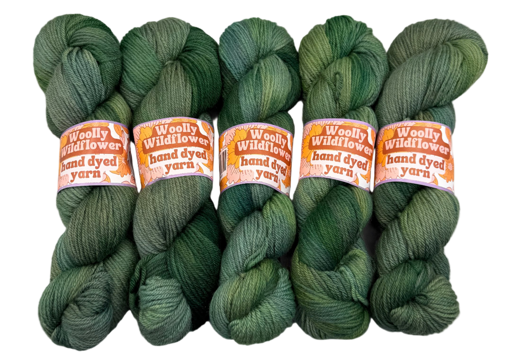 Five skeins of green yarn with orange labels on a white background