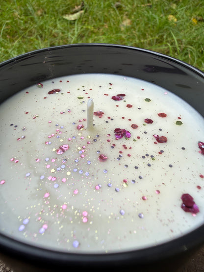 White candle with colorful sprinkles in a black container on grass