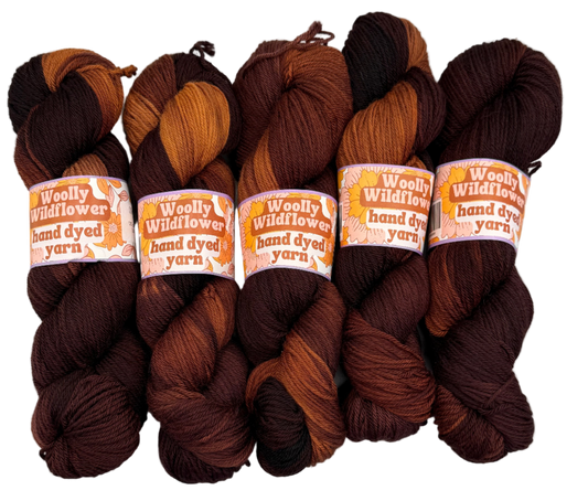 Five skeins of hand-dyed yarn in various brown shades on a white background with 'Woolly Wildflower' labels.