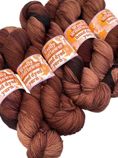 Brown yarn skeins with 'Woolly Wildflower' labels on a white background