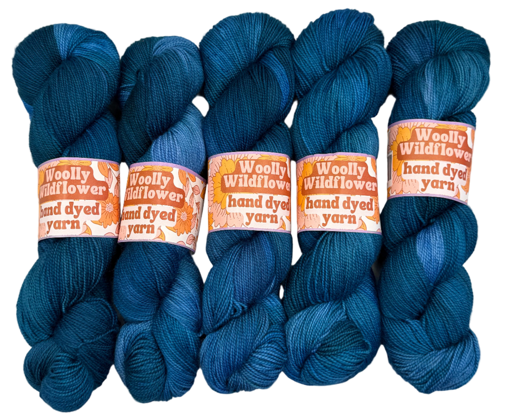 Five blue skeins of yarn with 'Woolly Wildflower' labels on a light gray background