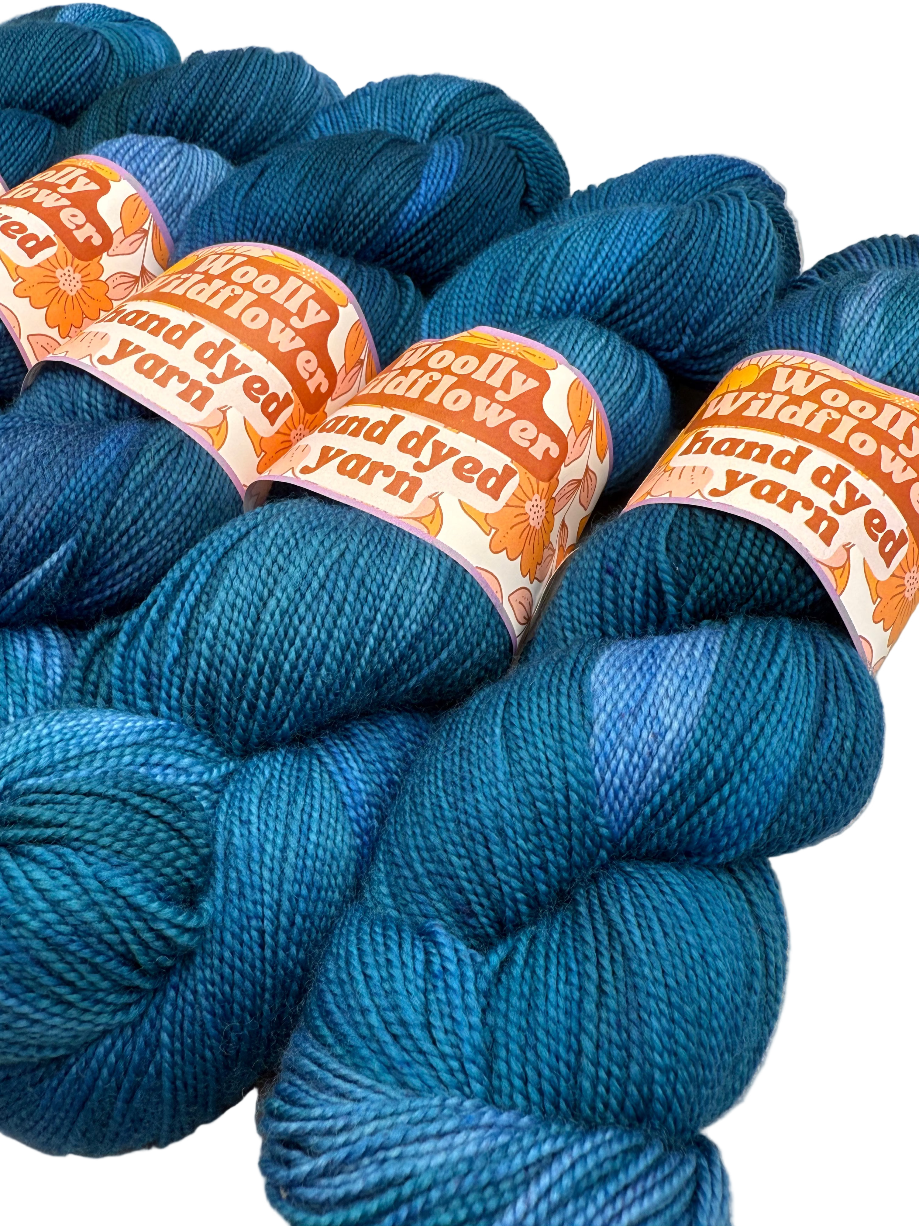Blue yarn skeins with 'Woolly Hand Dyed Yarn' labels on a light background