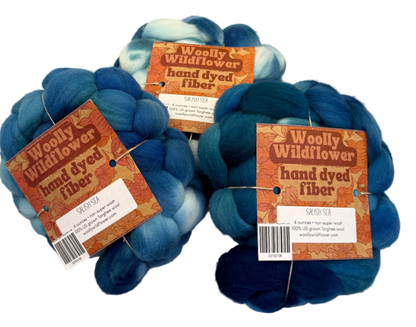 Three balls of blue and greens fiber with 'Woolly Wildflower' labels on a light gray background