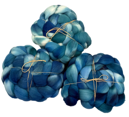 Three skeins of blue and green fibers tied with string on a light background