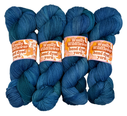 Four blue skeins of yarn with 'Woolly Wildflower' labels on a light gray background