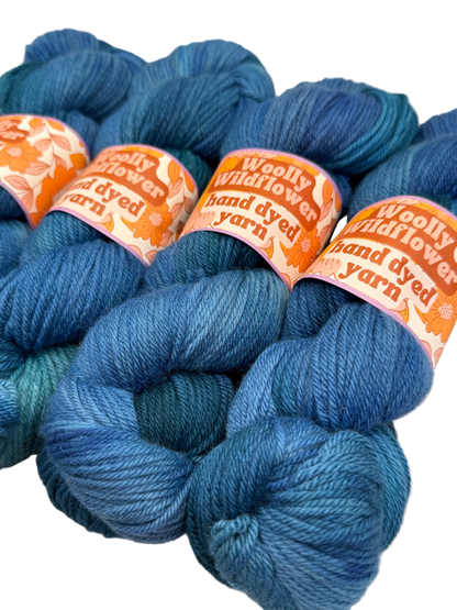 Blue yarn skeins with 'Woolly Wildflower' labels on a light background