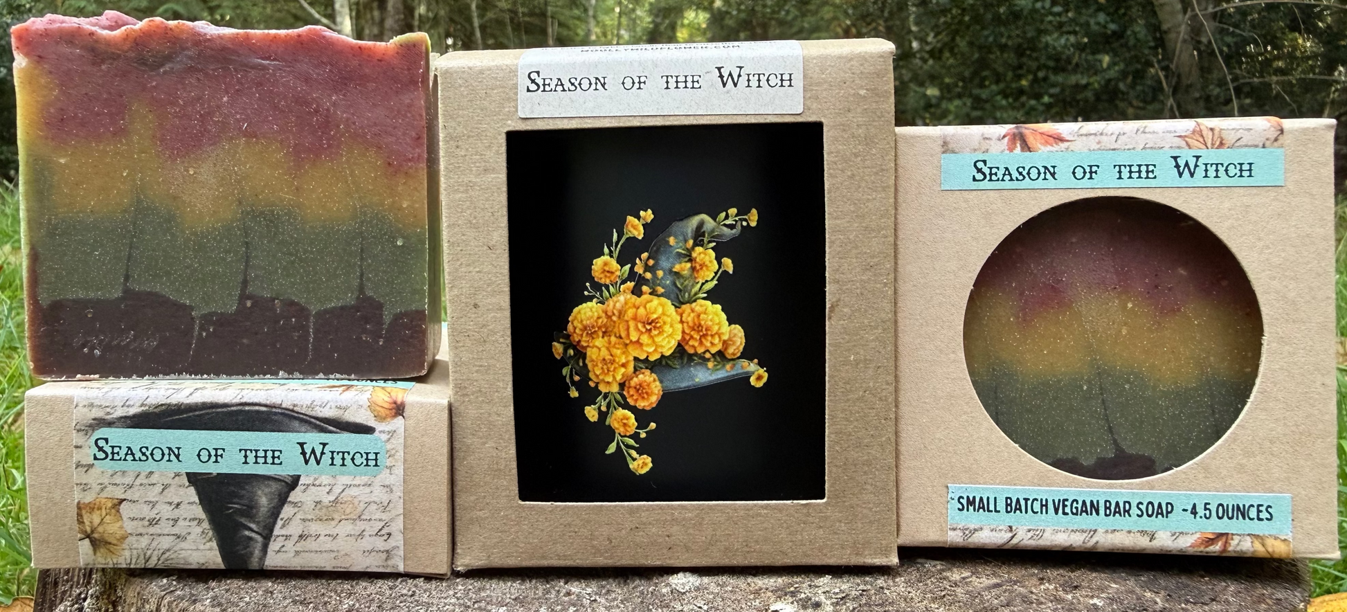 Three 'Season of the Witch' soap bars and packaging on a wooden log with a natural background.