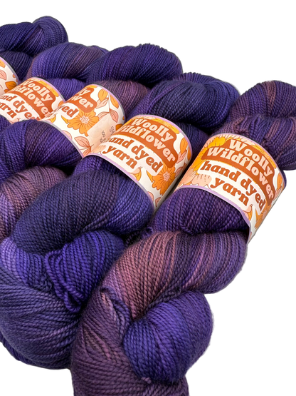 Purple yarn skeins with 'Woolly Wildflower Yarn' labels on a light gray background