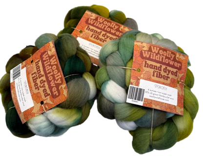 Three skeins of hand-dyed fiber in green and brown tones with 'Woolly Wildflower' labels on a gray background.